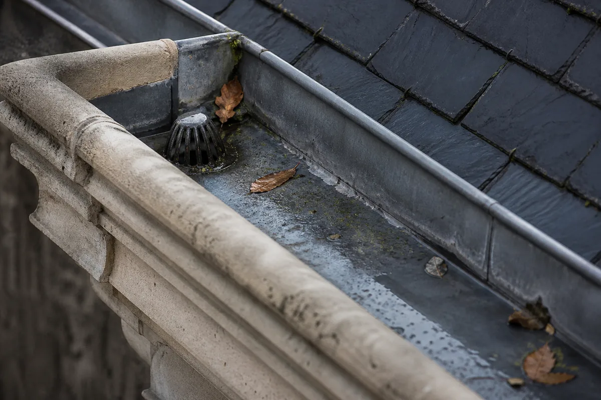 Chéneau en zinc encaissé derrière la corniche d’une maison de faubourg nantaise sous une pluie fine