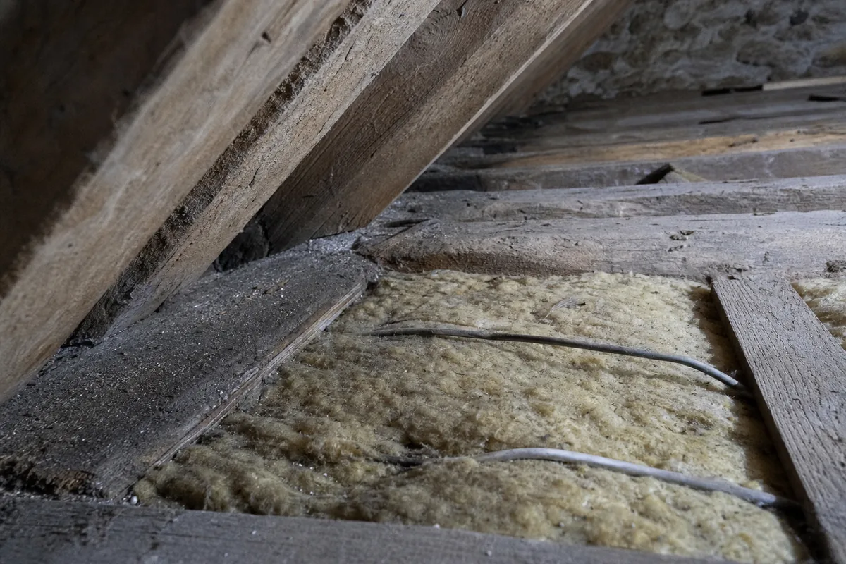 Combles perdus d’un pavillon nantais avec une ancienne laine de verre tassée entre les entraits d’une charpente fermette